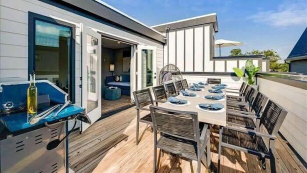 A modern outdoor dining area with a wooden deck, a barbecue grill, and a large table with chairs. - New, Luxury Home| Private Roof Deck (Nashville)