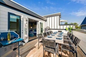 A modern outdoor dining area with a wooden deck, a barbecue grill, and a large table with chairs. - New, Luxury Home, Private Roof Deck (Nashville)