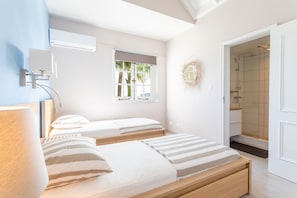 A bedroom with two beds, a window with a view, an air conditioning unit, and a shower area.