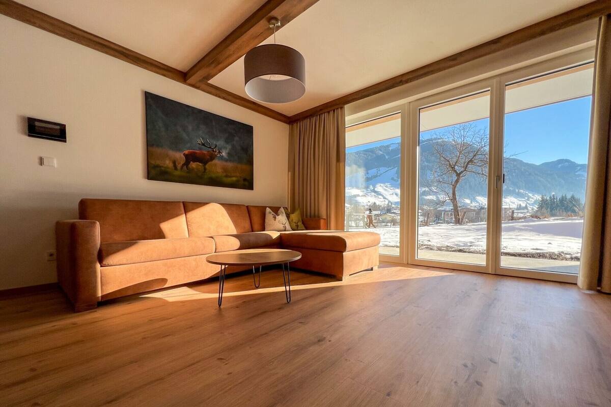 A modern living room with a wooden floor, a brown sofa, a round coffee table, and a large window with a mountain view.