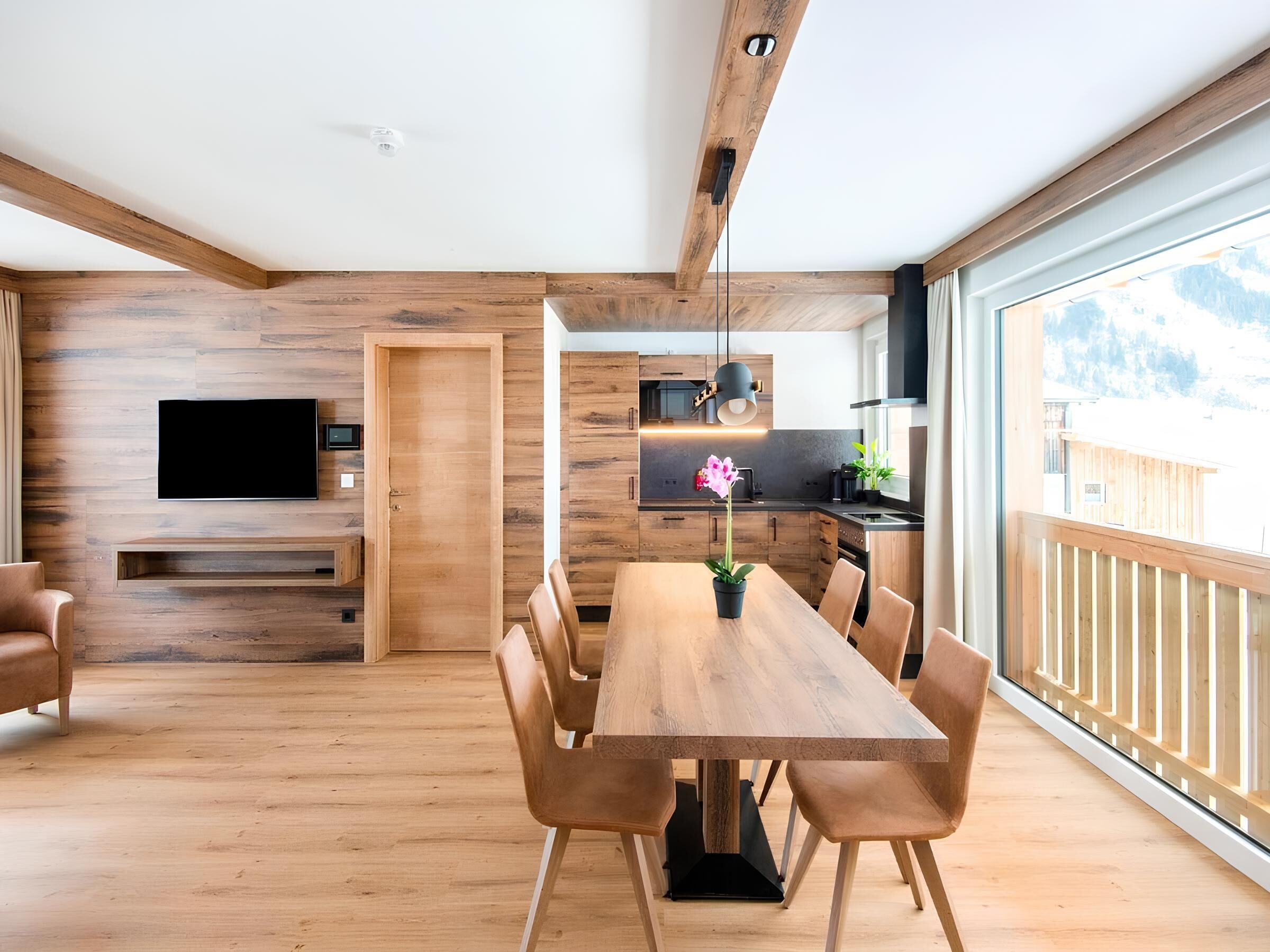 Une cuisine moderne avec des meubles en bois, un coin repas avec une table et des chaises en bois, et une grande fenêtre donnant sur l’extérieur.