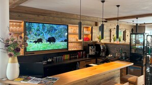 A modern kitchen with a wooden bar area, a large flat-screen TV, and pendant lighting.