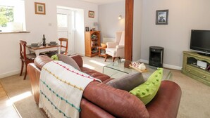 A living room with a leather sofa, a glass coffee table, a television, and a fireplace. - La'l Skaithe (Kirkby Stephen)