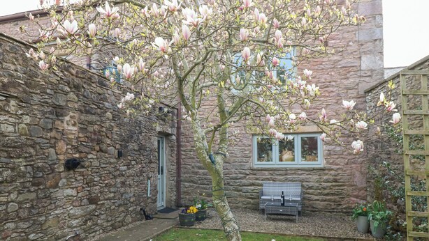 A stone building with a tree in the courtyard, a bench, and a small table with glasses. - La'l Skaithe (Kirkby Stephen)
