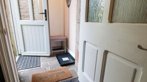 A narrow hallway with a white door, a small wooden bench, a black tray, and a doormat. - La'l Skaithe (Kirkby Stephen)
