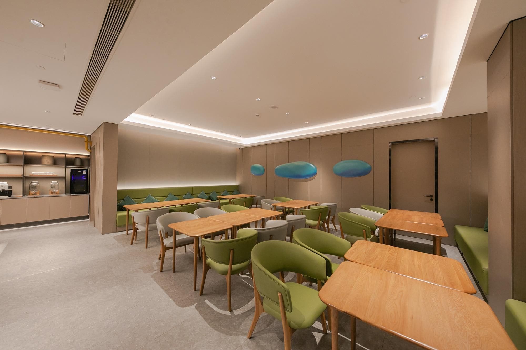 Un espace repas moderne avec des tables et des chaises, un coin cuisine équipé d’appareils électroménagers et un coin salon avec un banc.
