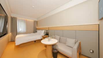 A hotel room with a bed, a sofa, a small round table, and a TV.