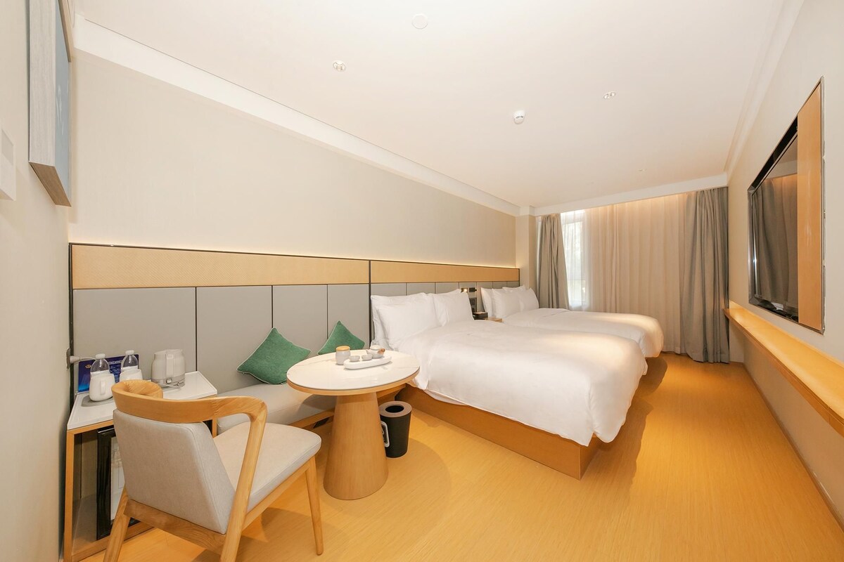 Une chambre d’hôtel avec deux lits, une petite table ronde, une chaise et une table de chevet équipée de divers accessoires.