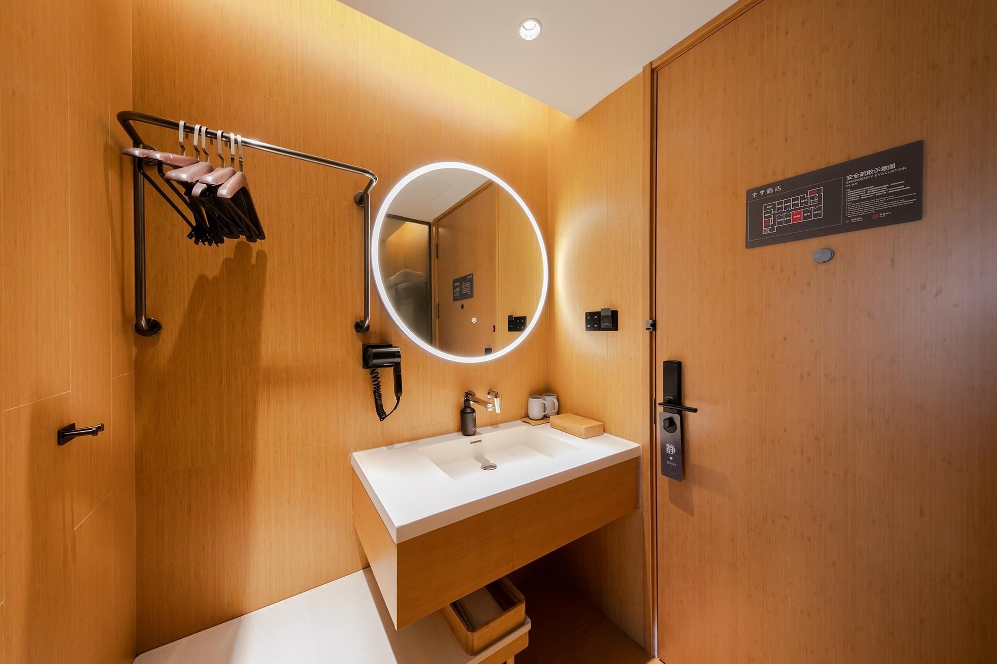 A modern bathroom with a wooden finish, a round mirror with lighting, a sink, and a towel rack.