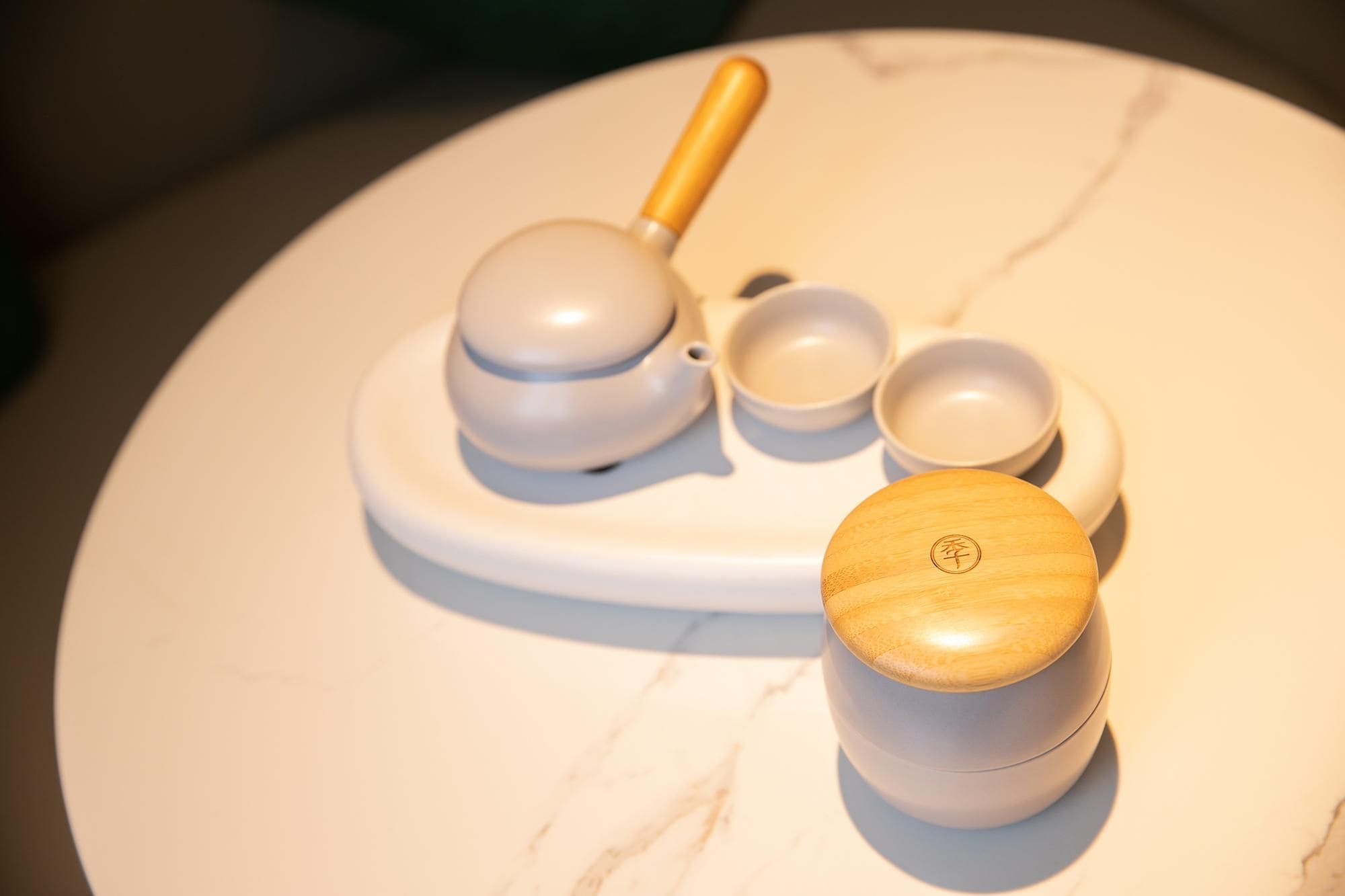 A white marble table with a tea set including a teapot, cups, and a wooden container with a lid.