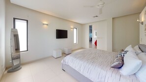 A modern bedroom with a large bed, a flat-screen TV, and a ceiling fan.