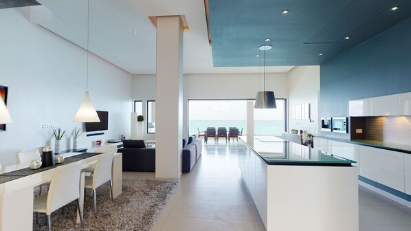 A modern kitchen with a central island, a dining area with a sofa, and a view of the ocean.