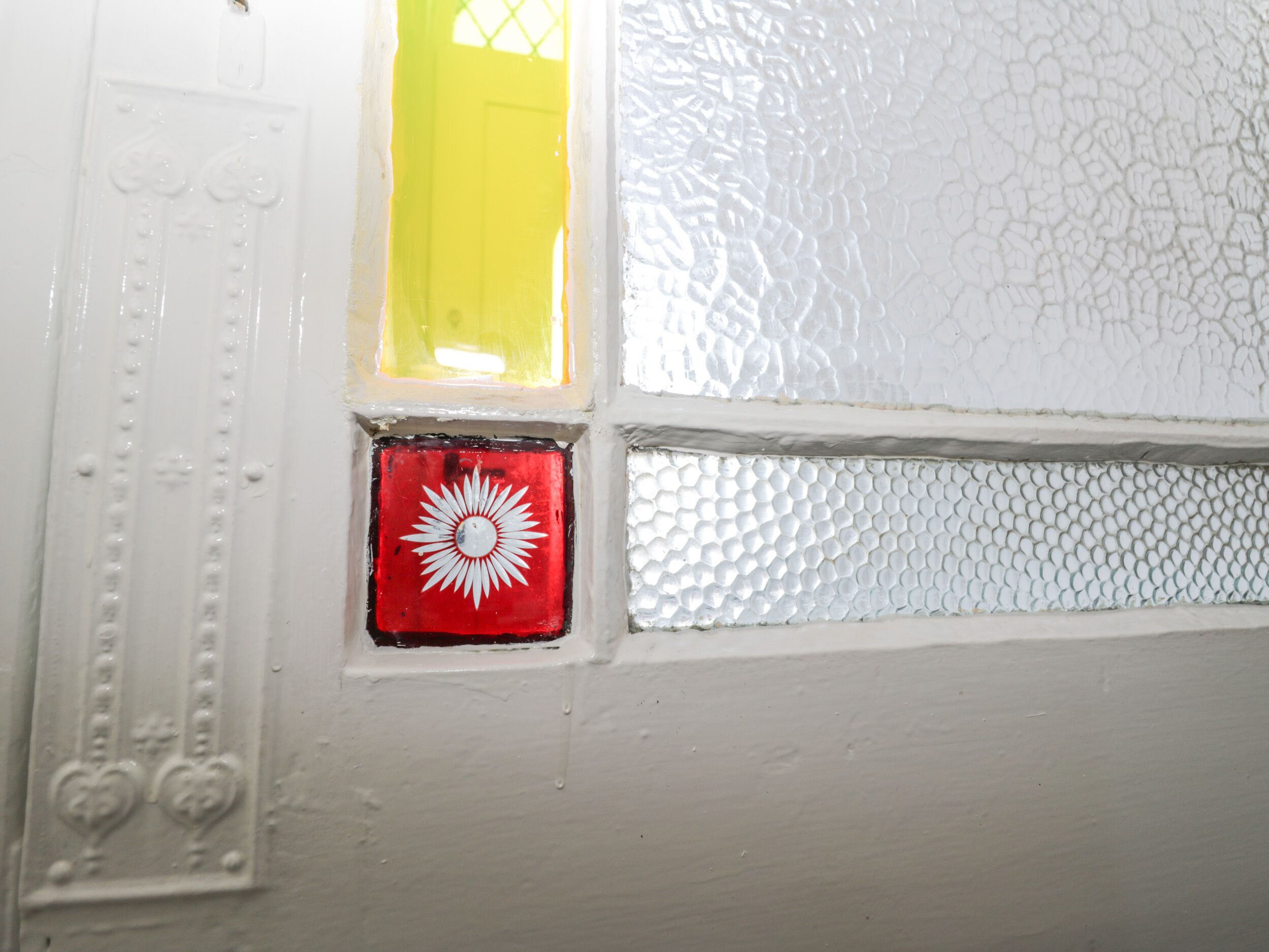 Una ventana con un letrero rojo y blanco, un panel de vidrio texturizado y una puerta blanca con molduras decorativas.