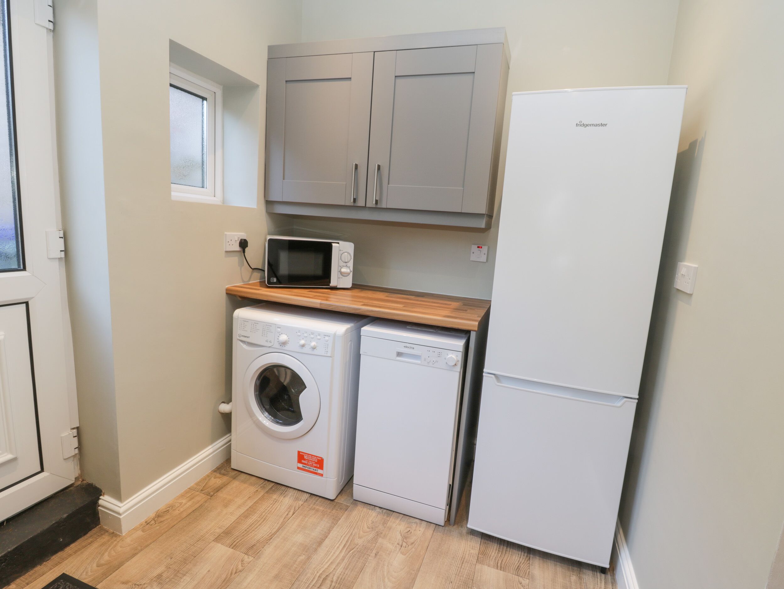 A compact kitchen with a washing machine, microwave, and refrigerator.