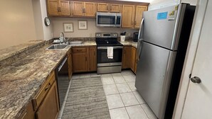 Una cocina con alacenas de madera, un refrigerador de acero inoxidable, un microondas, un horno y un lavamanos.