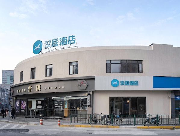 Un hôtel à la façade incurvée, une enseigne avec des caractères chinois et un vélo garé devant.