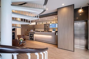 Un hall d’hôtel moderne comprenant un comptoir d’accueil, un espace salon et un escalier menant aux étages supérieurs.