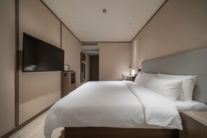 A hotel room with a large bed, a flat-screen TV, a bedside table, and a desk with a lamp.