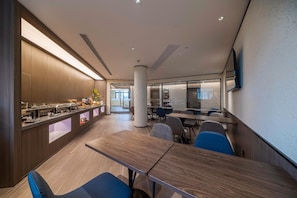 Un espace repas moderne avec une longue table en bois, des chaises bleues et un buffet proposant divers plats.