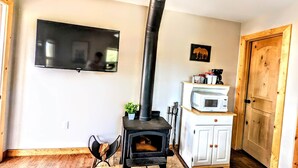 A cozy room with a wood-burning stove, a television mounted on the wall, and a wooden door. - # 3. Howling Wolf's Lair - Studio W/ Fireplace (Pet Free) (Santa Ysabel)