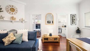 A living room with a sofa, a coffee table, a mirror, and a kitchen area in the background.