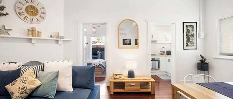 A living room with a sofa, a coffee table, a mirror, and a kitchen area in the background.