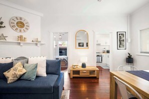 A living room with a sofa, a coffee table, a mirror, and a kitchen area in the background.