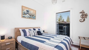A bedroom with a bed, bedside table, nightstand, artwork, and a view of the outdoors.