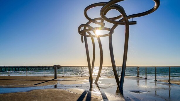 A metal sculpture with rings, a pier, and the ocean in the background.