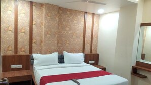 A hotel room with a bed, wooden headboard, a ceiling fan, and a mirror on the wall. - Hotel Red Rose (Vadodara)