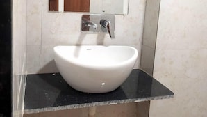 A bathroom with a white sink, a mirror, and a black countertop. - Hotel Red Rose (Vadodara)