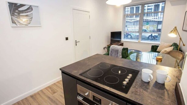 A modern kitchen with a built-in stove, a dining area with a glass table, and a view of the street through a window.