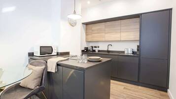 A modern kitchen with a central island, a microwave, and a dining area with a glass table and a chair.