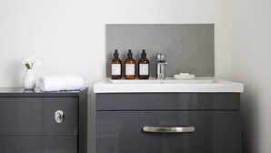 A bathroom vanity with a white countertop, three bottles of toiletries, a white vase with flowers, and a towel.