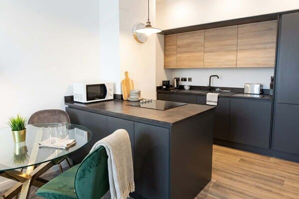 A modern kitchen with a central island, dark cabinetry, and a glass dining table with a green chair.