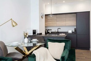 A modern kitchen with a microwave, sink, and dark cabinets. There is a dining table with chairs and a lamp.