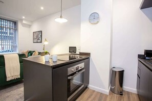A compact kitchen with a built-in oven, a small island with a coffee maker, and a trash can.