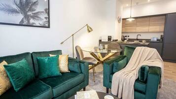 A modern living room with a green sofa, a coffee table, and a dining area with a glass table.
