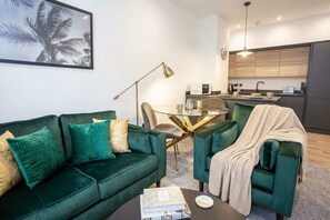 Una sala de estar moderna con un sofá verde, una mesa de centro y un comedor con una mesa de vidrio.