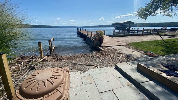 Een terras aan het meer met een houten steiger die in het water reikt, een overdekt zitgedeelte en een betonnen pad naar de waterlijn.