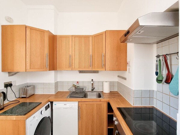 Compact kitchen with dishwasher, stovetop, oven, sink, toaster, and kettle.