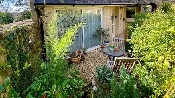 Une petite maisonnette accueillante, avec un toit en tuiles, une porte vitrée donnant sur un patio et une petite table entourée de chaises.