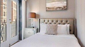 A hotel room with a large bed, a bedside lamp, a framed artwork on the wall, and a view of the outside through a door.