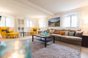 Un salon spacieux avec un grand canapé, deux fauteuils jaunes, une table basse et une bibliothèque.