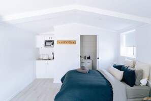 A modern bedroom with a large bed, a built-in wardrobe, and a kitchenette in the background. - Seagrass (Culburra Beach)