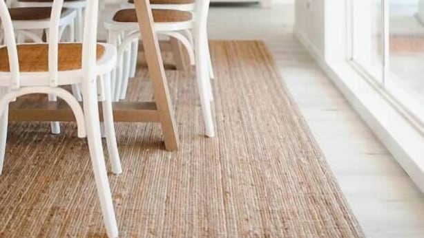 Un espace repas moderne avec des chaises blanches et une table en bois, un tapis tissé et un tableau accroché au mur.