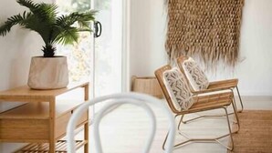 Un salon moderne avec une table en bois, des chaises blanches, une plante en pot et une décoration murale tissée.