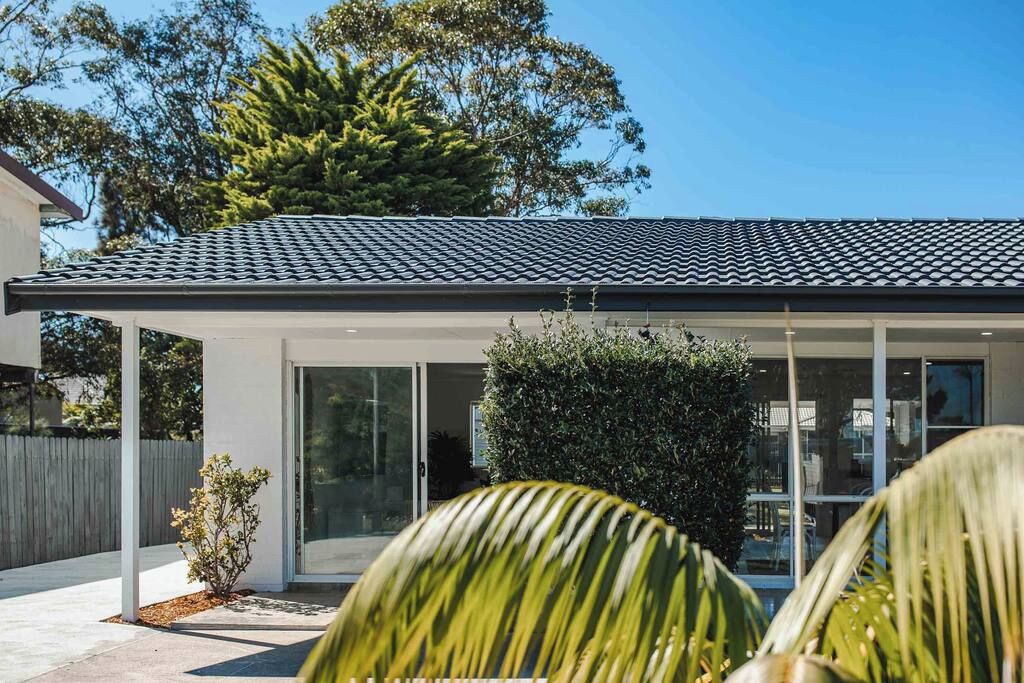A modern house with a tiled roof, large glass windows, and a covered patio area.