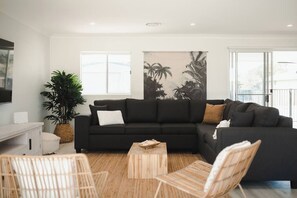 Un salon moderne avec un canapé d’angle noir, une table basse en bois et une grande plante.