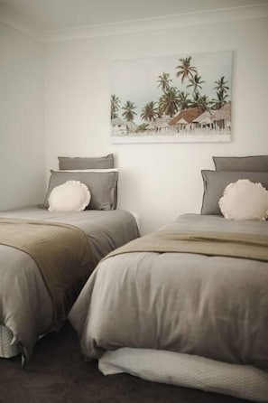 A bedroom with two beds, each with a pillow and a blanket. There is a painting on the wall above the beds. - Seagrass (Culburra Beach)